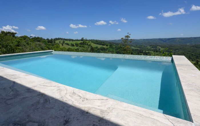 A Pool Overlooking Green Hills and Blue Sky, with White Stone Deck — Mad Pool Interiors and Renovations in Baringa, QLD