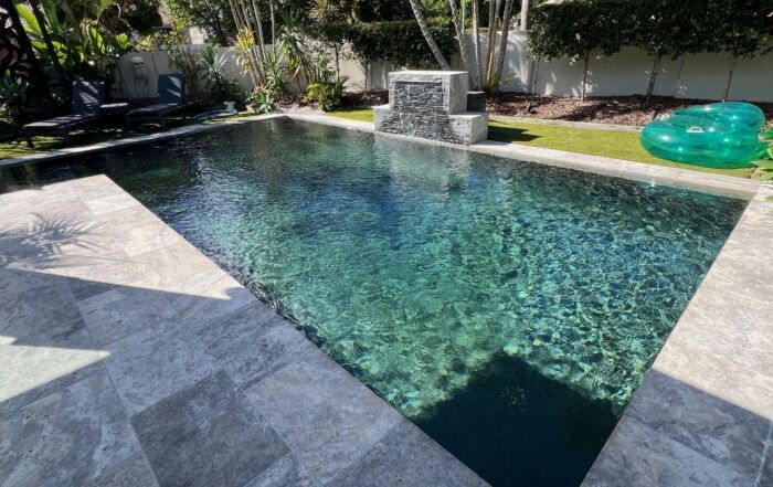 Modern Backyard Swimming Pool with Clear Water, Stone Deck, and A Small Waterfall Feature — Mad Pool Interiors and Renovations in Baringa, QLD