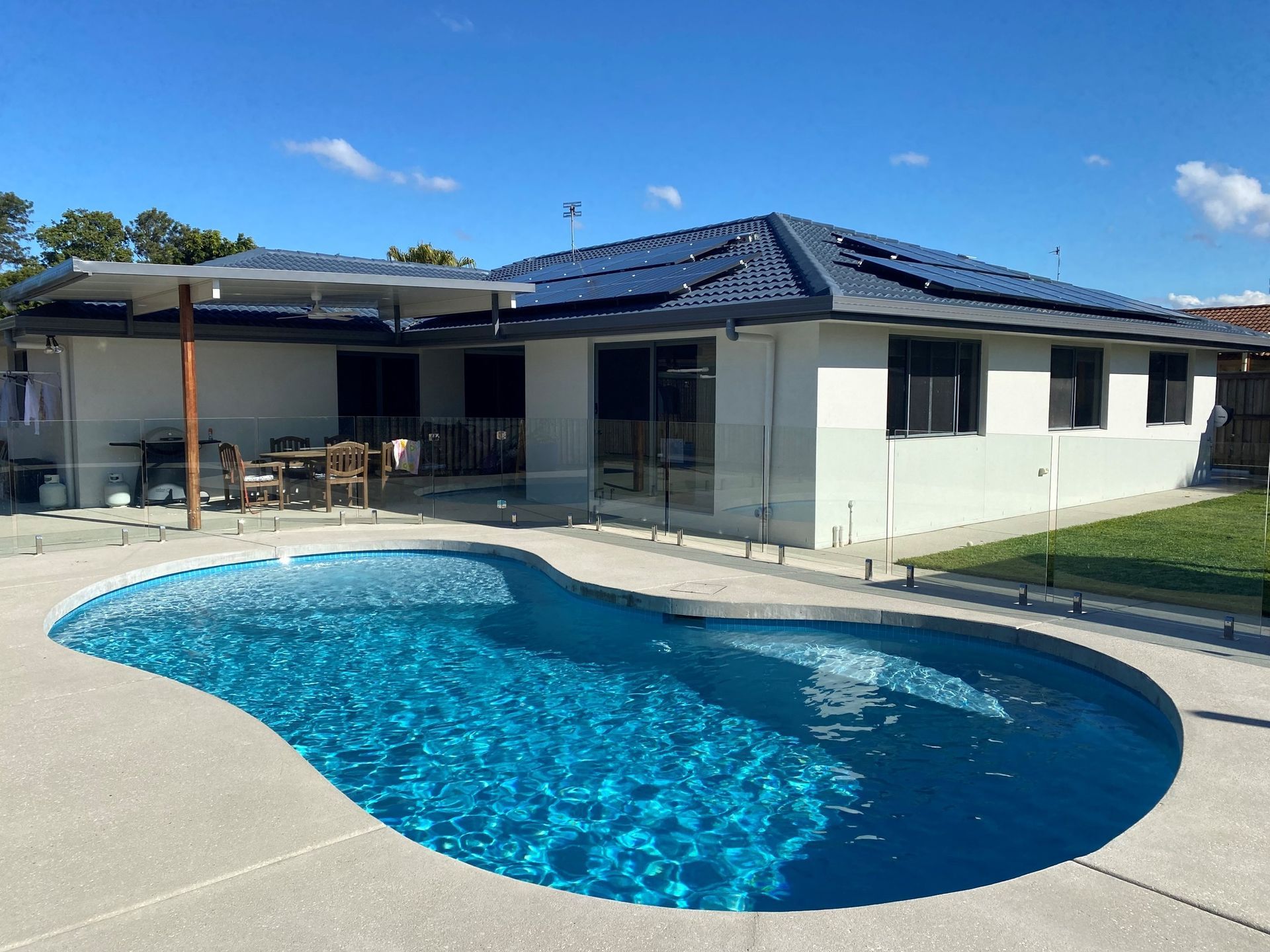 Backyard With a Blue, Freeform Pool, Patio, and House With Solar Panels — Mad Pool Interiors and Renovations in Baringa, QLD