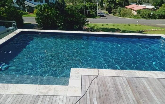 Blue Swimming Pool Beside a Wooden Deck — Mad Pool Interiors and Renovations in Baringa, QLD