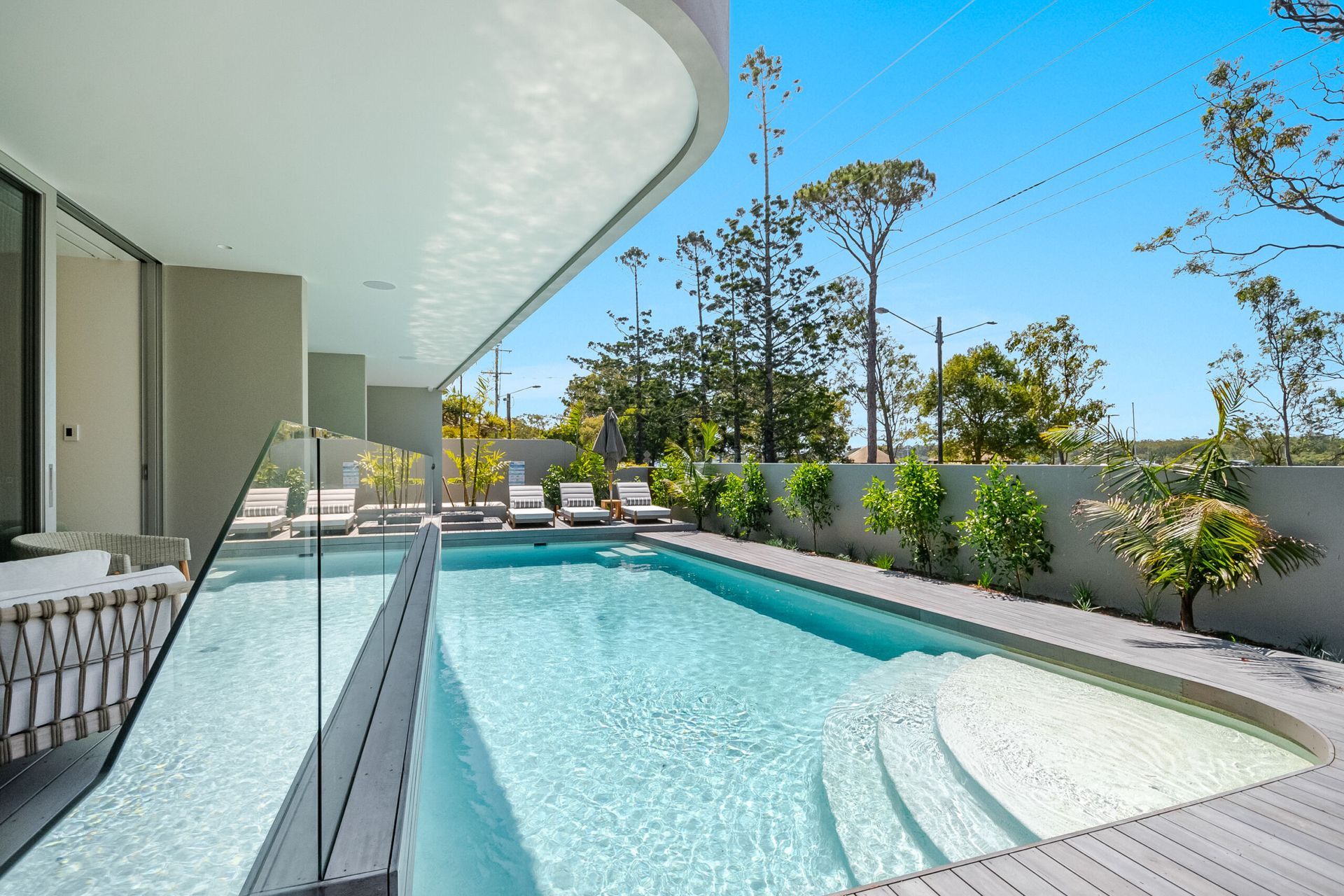 Pool With Steps, Glass Railing, Lounge Chairs, and an Overhanging Roof — Mad Pool Interiors and Renovations in Baringa, QLD