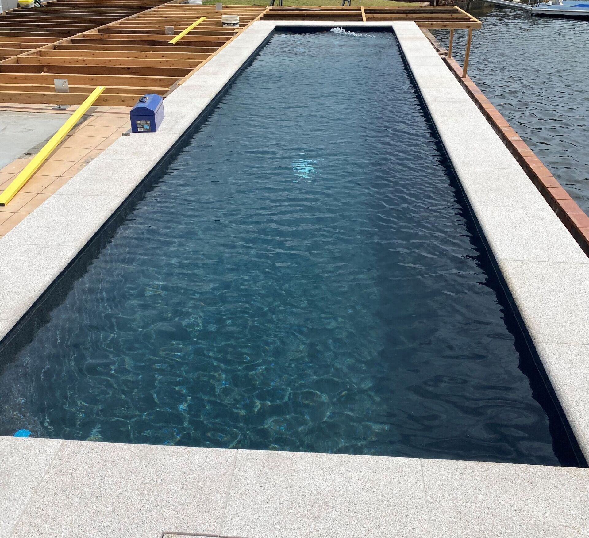 Long, Rectangular Pool With Dark Water, Light Stone Border — Mad Pool Interiors and Renovations in Baringa, QLD