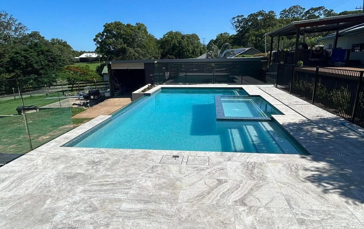 Backyard Swimming Pool with Blue Water, Concrete Deck, and Trees — Mad Pool Interiors and Renovations in Baringa, QLD