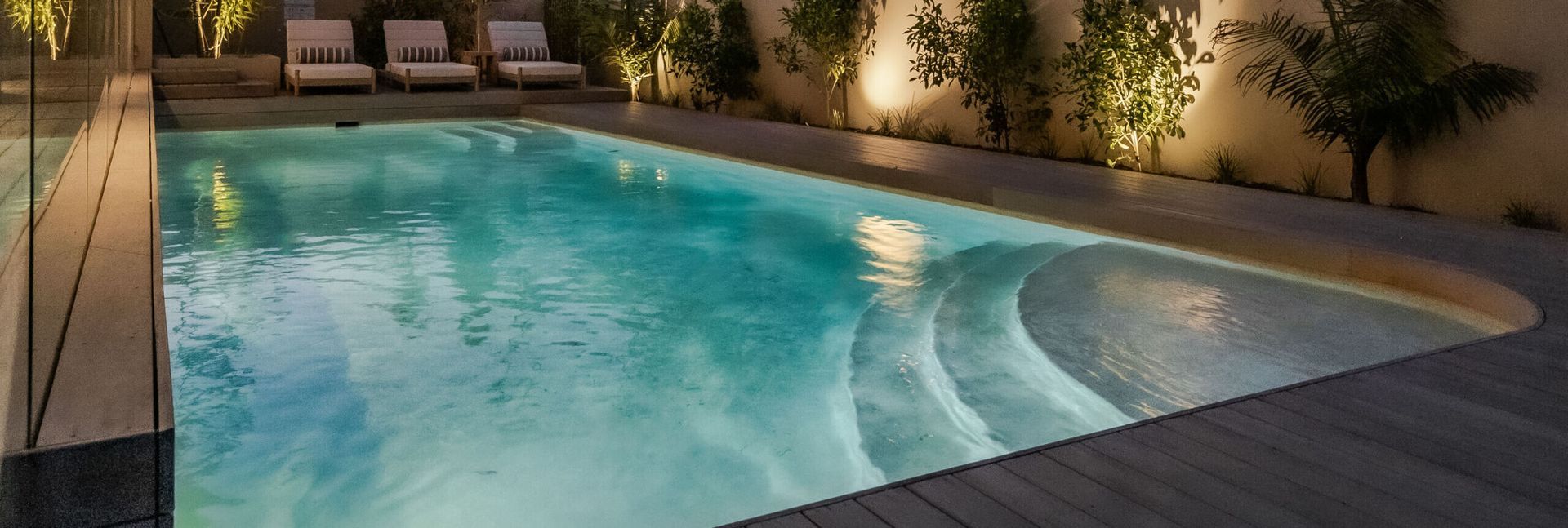 Illuminated Swimming Pool With Steps, Surrounded by Wooden Deck — Mad Pool Interiors and Renovations in Baringa, QLD