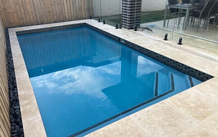 Rectangular Backyard Pool with Blue Water, Tiled Deck, and Glass Patio Railing — Mad Pool Interiors and Renovations in Baringa, QLD