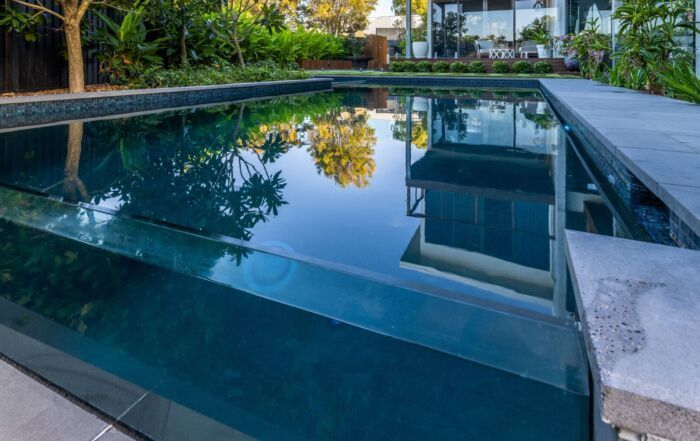 Modern Backyard Swimming Pool with Blue Water Reflecting Trees and A House — Mad Pool Interiors and Renovations in Baringa, QLD