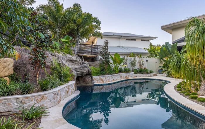 Lush Backyard Pool with Rock Waterfall, Tropical Plants, and A Curved Stone Deck — Mad Pool Interiors and Renovations in Baringa, QLD