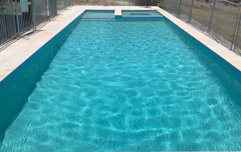 Outdoor Swimming Pool with Clear Blue Water and Surrounding Metal Fencing — Mad Pool Interiors and Renovations in Baringa, QLD