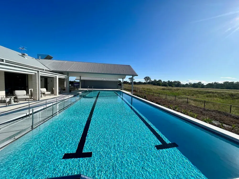 Long, Clear Swimming Pool Next to a House Under a Blue Sky — Mad Pool Interiors and Renovations in Baringa, QLD