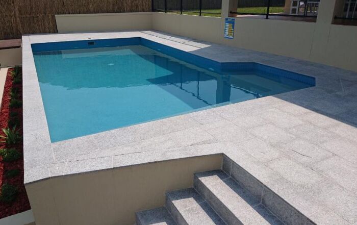 Modern White-Tiled Swimming Pool with Blue Water and Steps in The Foreground — Mad Pool Interiors and Renovations in Baringa, QLD