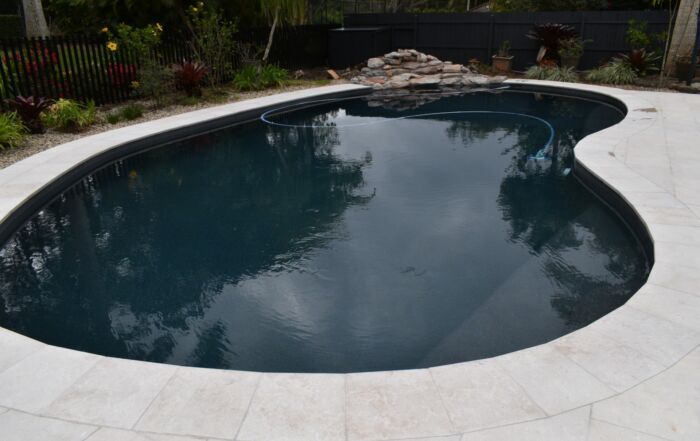 Kidney-Shaped Backyard Swimming Pool with Water and Light Stone Deck — Mad Pool Interiors and Renovations in Baringa, QLD