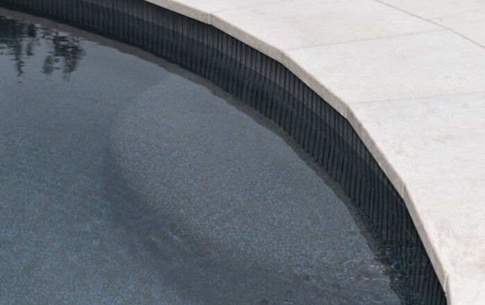 Curved Swimming Pool Edge with Dark Water Beside Light Concrete Decking — Mad Pool Interiors and Renovations in Baringa, QLD