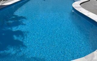 Curved Blue Swimming Pool with White Stone Edges — Mad Pool Interiors and Renovations in Baringa, QLD