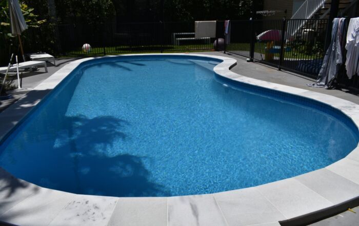Backyard Swimming Pool with Blue Water, White Deck, and Lounge Chairs — Mad Pool Interiors and Renovations in Baringa, QLD