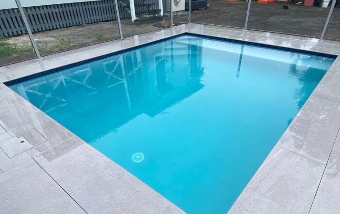 Rectangular Outdoor Swimming Pool with Clear Blue Water Surrounded by Light Gray Tiles — Mad Pool Interiors and Renovations in Baringa, QLD
