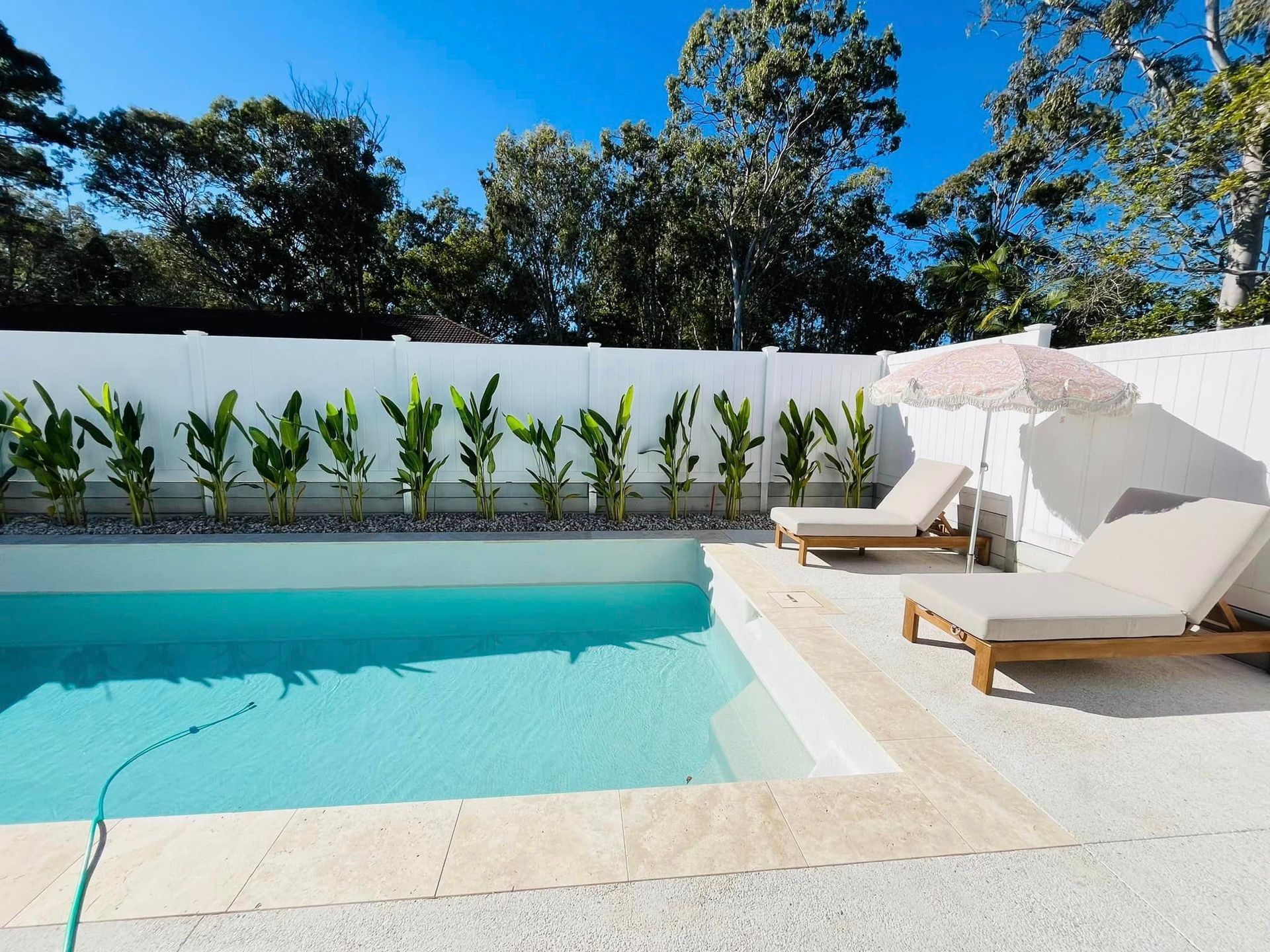 Poolside Scene With a Pool, Two Lounge Chairs, and a Pink Umbrella — Mad Pool Interiors and Renovations in Baringa, QLD