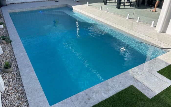 Rectangular Turquoise Swimming Pool with White Stone Deck and Surrounding Grass — Mad Pool Interiors and Renovations in Baringa, QLD