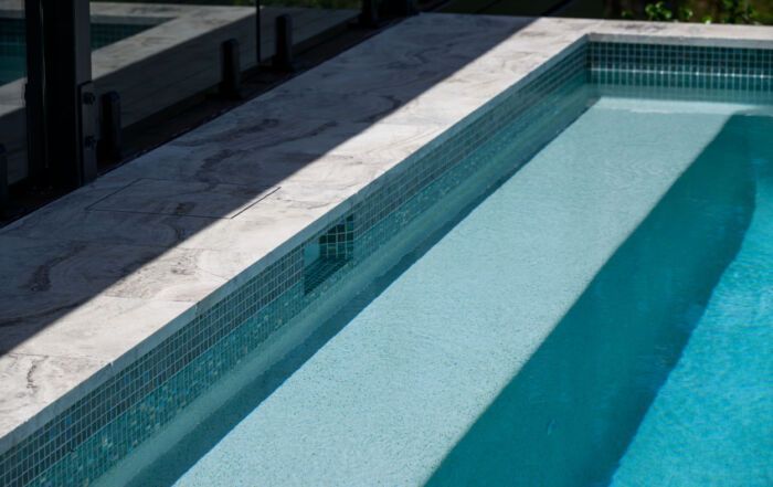 Empty Swimming Pool with Light Blue Water and Tiled Edge Beside a Sunlit Deck — Mad Pool Interiors and Renovations in Baringa, QLD
