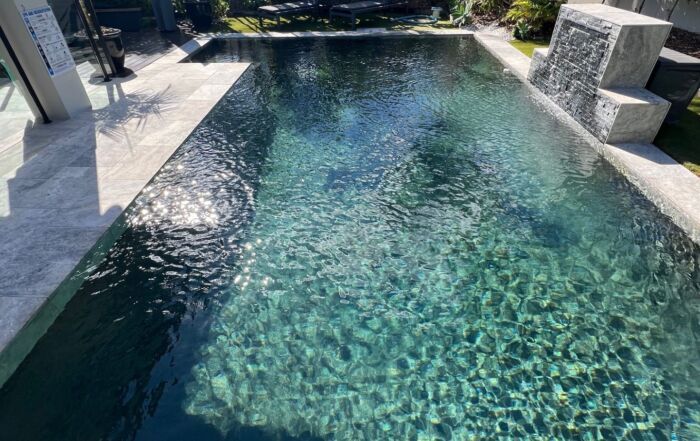 Modern Backyard Swimming Pool with Clear Blue Water, Stone Deck, and Shaded Seating Area — Mad Pool Interiors and Renovations in Baringa, QLD