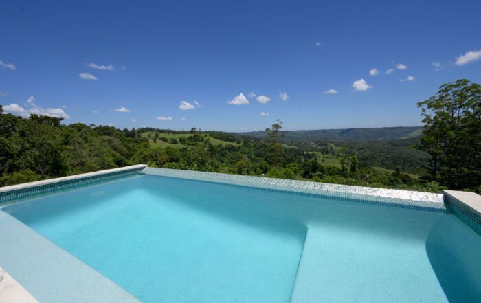 Infinity Pool Overlooking Lush Green Hills Under a Blue Sky — Mad Pool Interiors and Renovations in Baringa, QLD