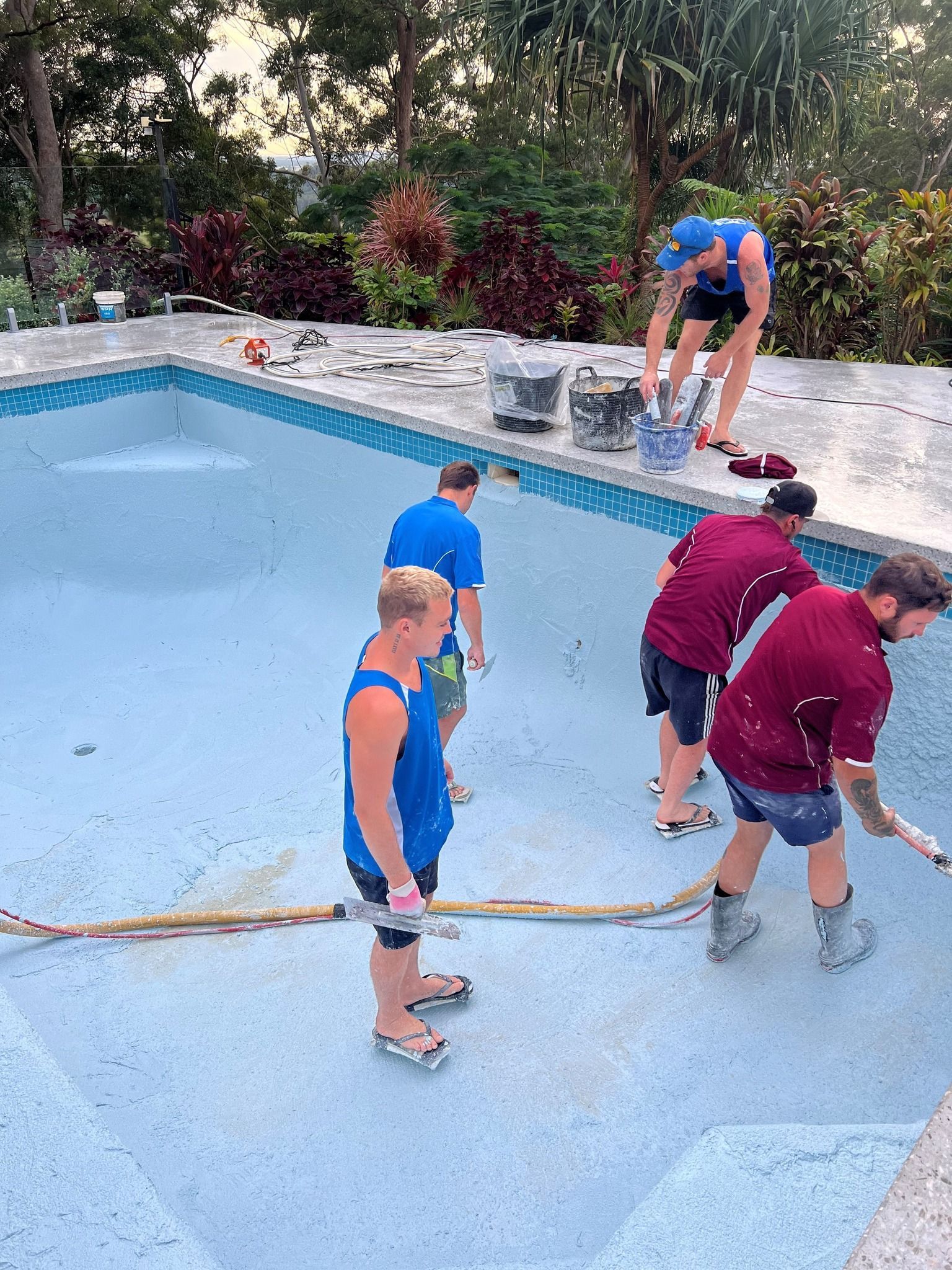 Five people are working on cleaning an empty swimming pool — Mad Pool Interiors and Renovations in Baringa, QLD