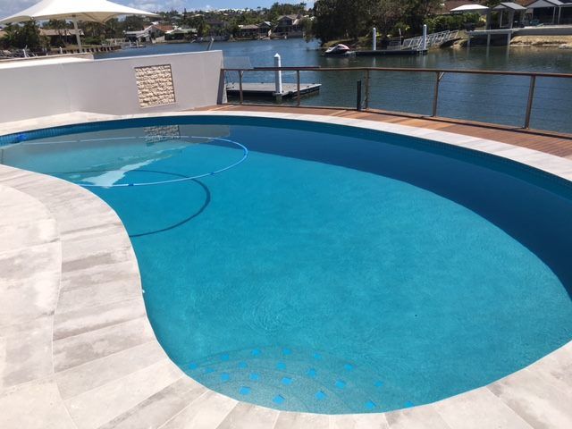 Curved Blue Swimming Pool Overlooking a Calm Waterfront — Mad Pool Interiors and Renovations in Baringa, QLD