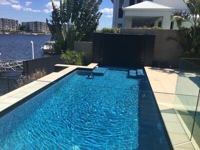 Long Blue Pool Beside a Waterfront Patio — Mad Pool Interiors and Renovations in Baringa, QLD