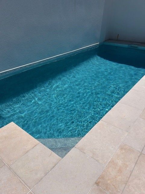 Blue Tiled Pool Beside Beige Stone Patio and Wall Corner — Mad Pool Interiors and Renovations in Baringa, QLD
