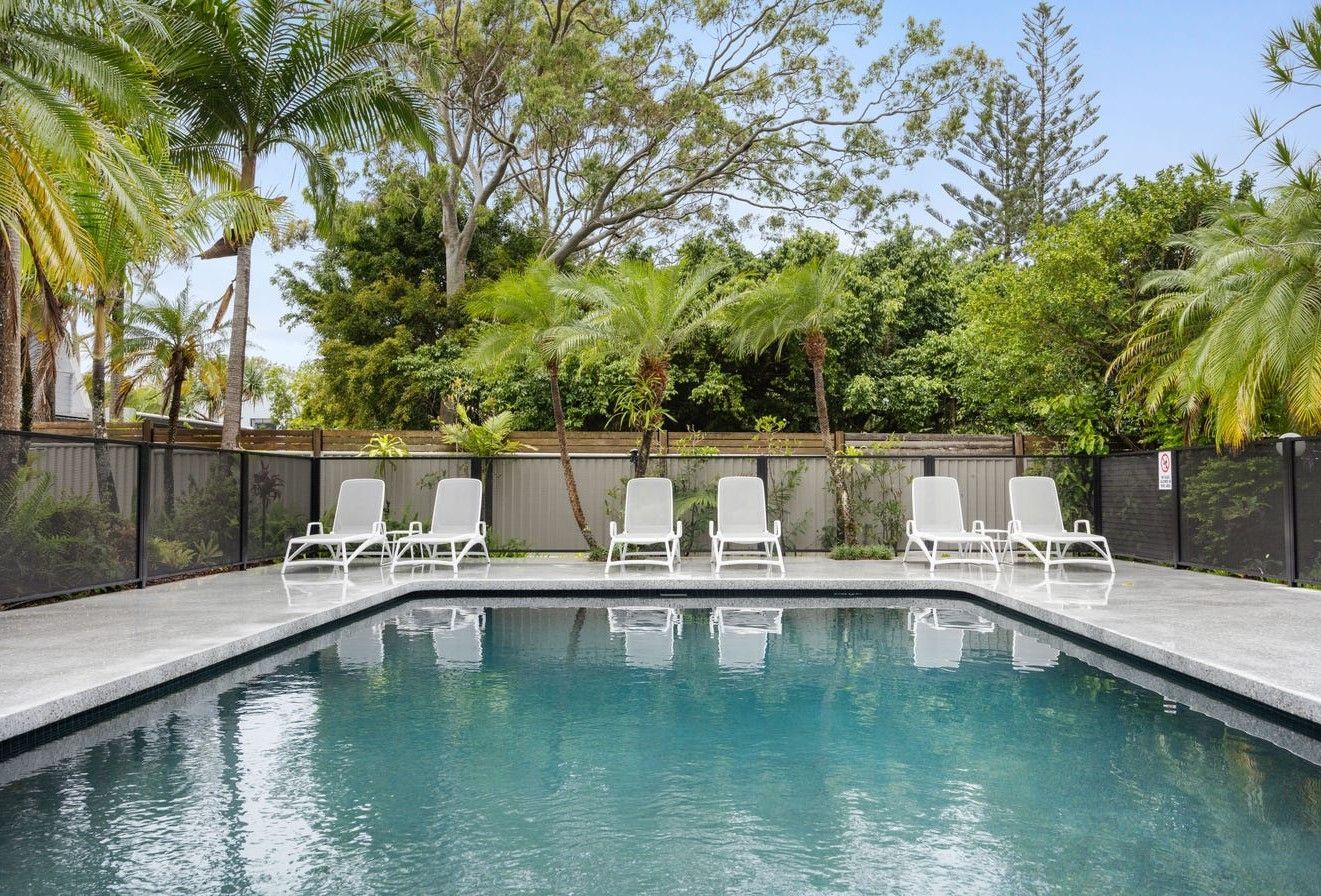 A Rectangular Swimming Pool Surrounded by White Lounge Chairs — Mad Pool Interiors and Renovations in Baringa, QLD