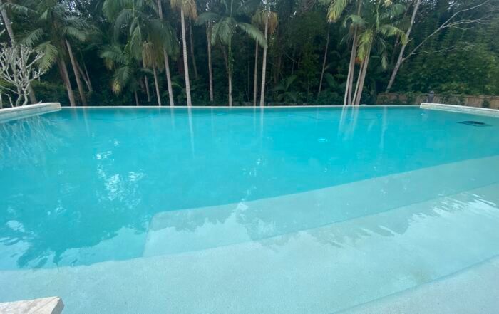 Turquoise Swimming Pool with Shallow Steps, Surrounded by Lush Tropical Greenery — Mad Pool Interiors and Renovations in Baringa, QLD