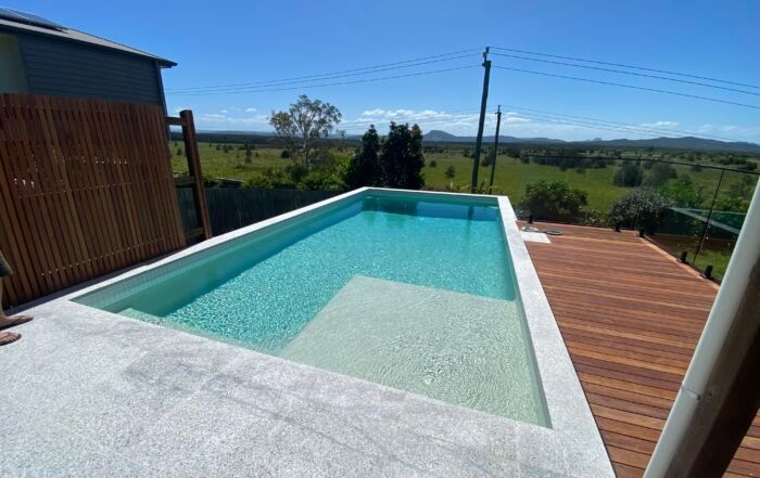 Backyard Infinity Pool Beside a Wooden Deck — Mad Pool Interiors and Renovations in Baringa, QLD