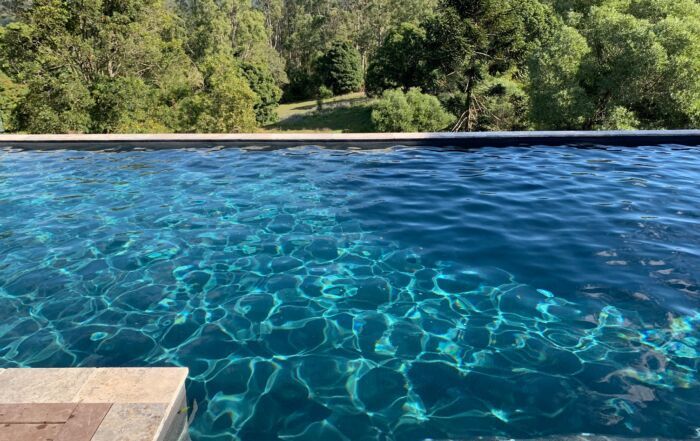 Blue Infinity Pool with Rippling Water and Lush Green Trees — Mad Pool Interiors and Renovations in Baringa, QLD