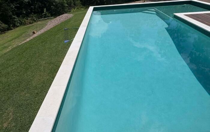 Turquoise Swimming Pool Beside a Green Lawn and White Pool Coping — Mad Pool Interiors and Renovations in Baringa, QLD
