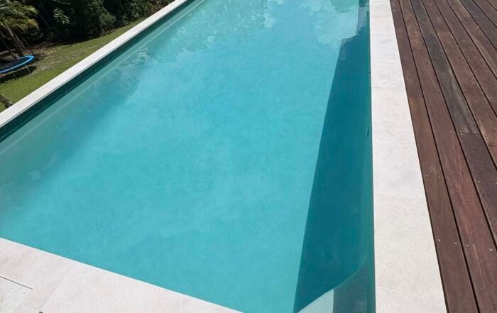 Long Rectangular Turquoise Swimming Pool Beside a Wooden Deck and White Border — Mad Pool Interiors and Renovations in Baringa, QLD
