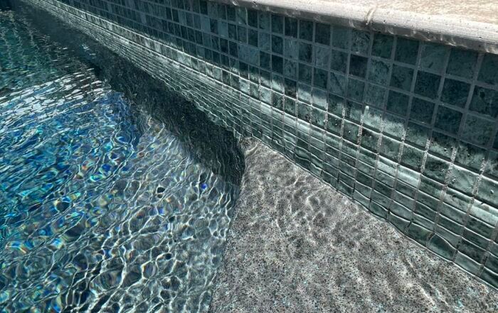 Sunlit Swimming Pool Corner with Blue-And-Gray Mosaic Tiles and Rippling Water — Mad Pool Interiors and Renovations in Baringa, QLD
