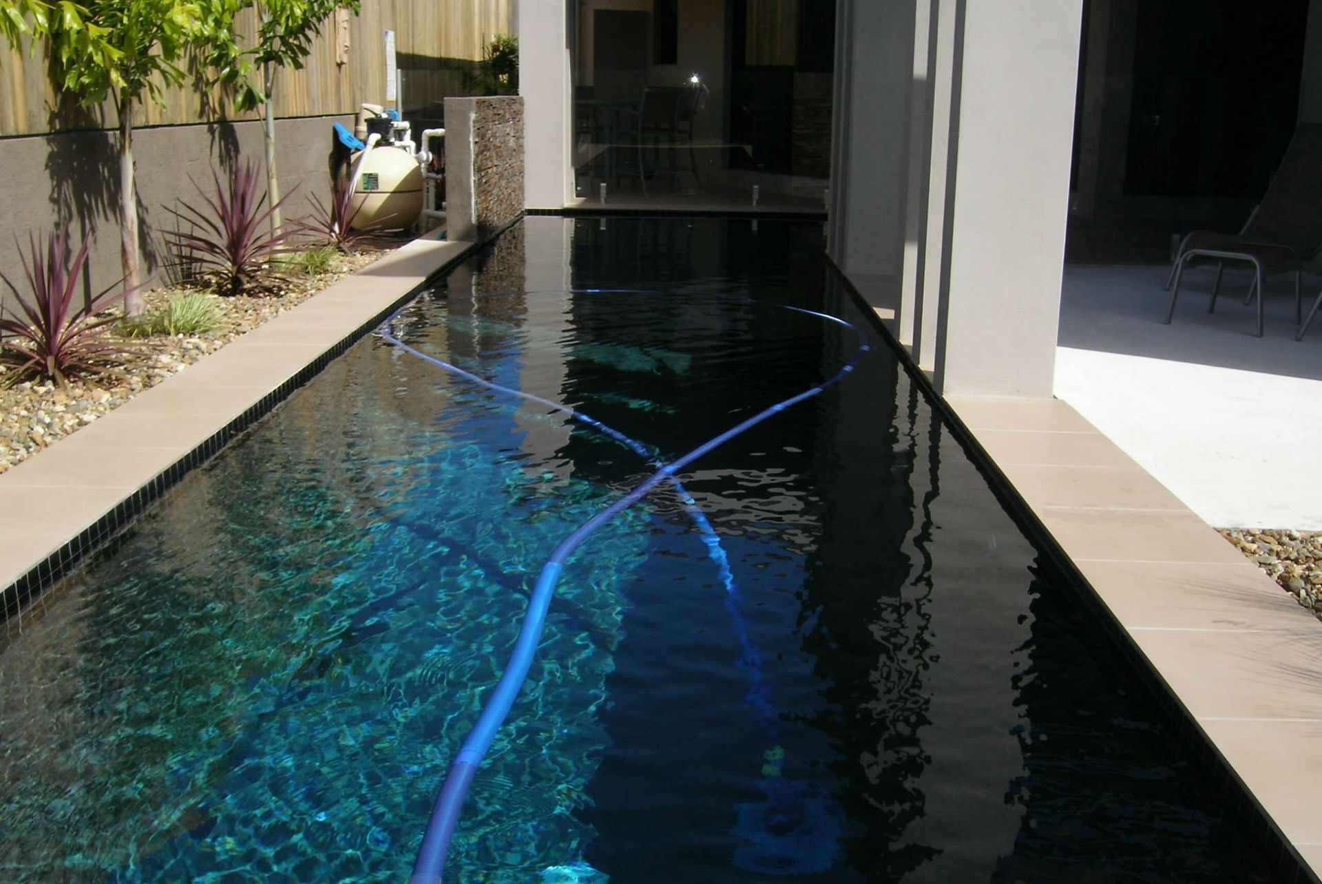 Long, Rectangular Swimming Pool With Dark Water and a Blue Cleaning Hose — Mad Pool Interiors and Renovations in Baringa, QLD