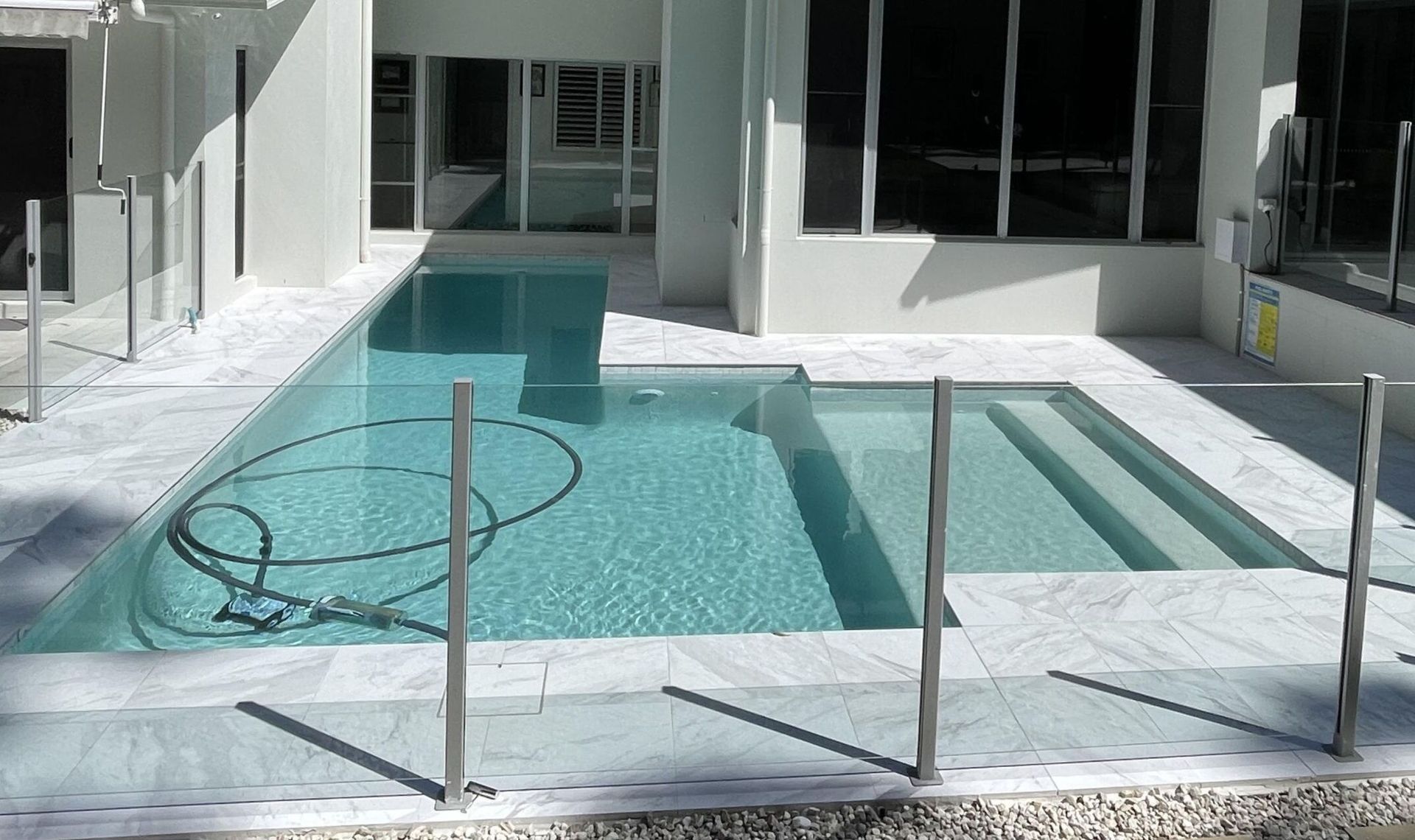 Modern White Patio With a Turquoise Pool and Glass Safety Fence — Mad Pool Interiors and Renovations in Baringa, QLD