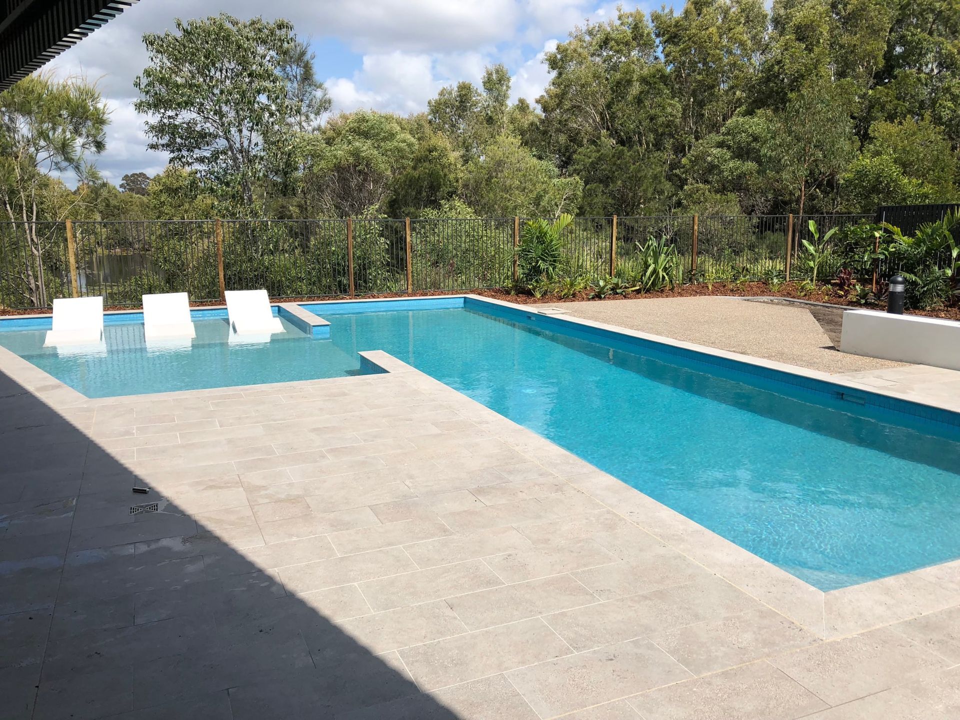 Swimming Pool With Three White Lounge Chairs in a Shallow Area — Mad Pool Interiors and Renovations in Baringa, QLD