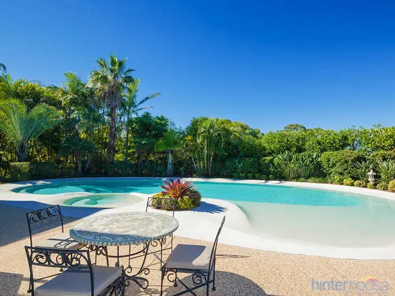 Tropical Resort Pool With a Round Table and Chairs on a Sunny Patio — Mad Pool Interiors and Renovations in Baringa, QLD