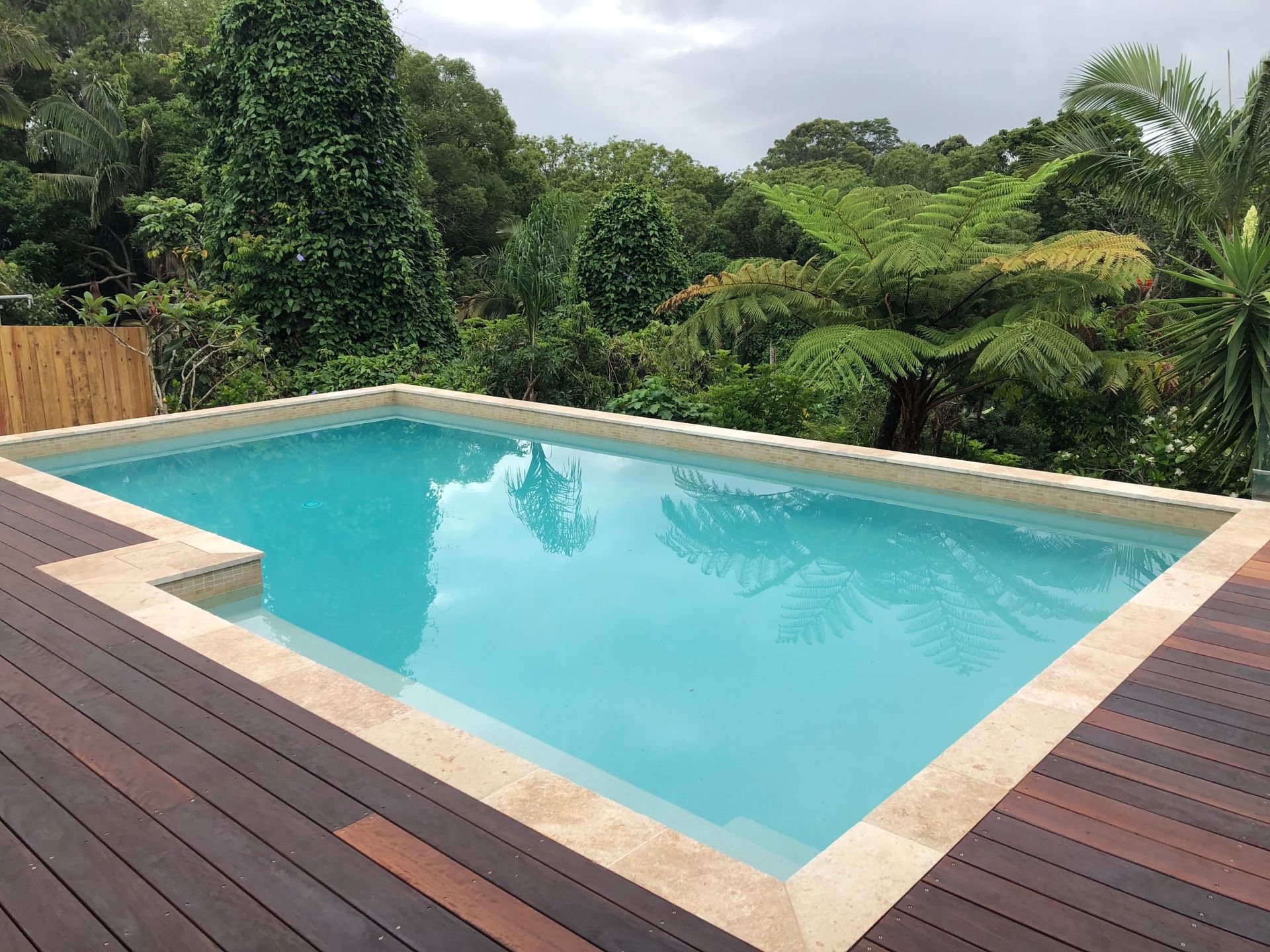 Swimming Pool With Blue Water and Wooden Deck — Mad Pool Interiors and Renovations in Baringa, QLD