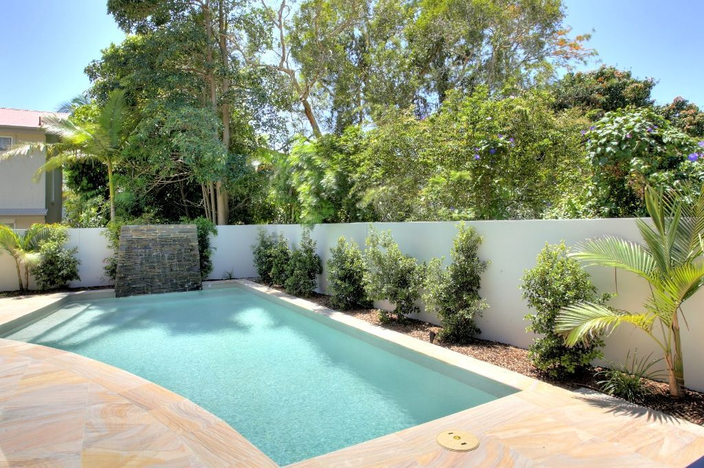 Pool With Waterfall Feature, White Wall, Green Foliage, and Blue Sky — Mad Pool Interiors and Renovations in Baringa, QLD