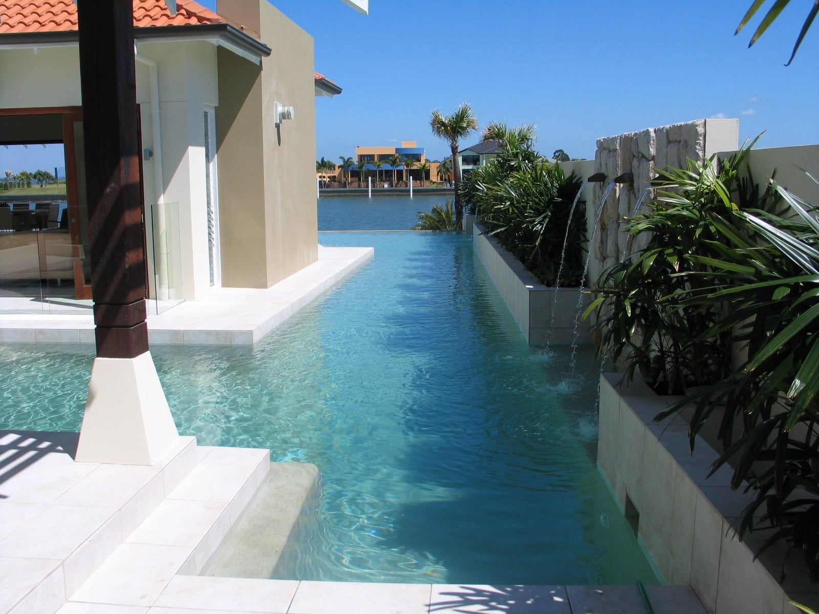 A Narrow, Turquoise Infinity Pool Alongside a House — Mad Pool Interiors and Renovations in Baringa, QLD