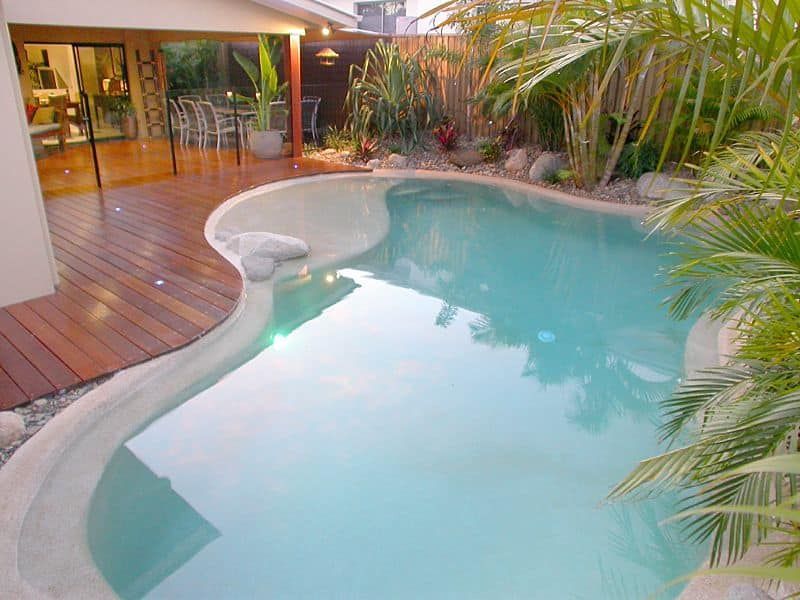 Pool Area With Turquoise Water, Wood Deck, and Lush Tropical Plants — Mad Pool Interiors and Renovations in Baringa, QLD