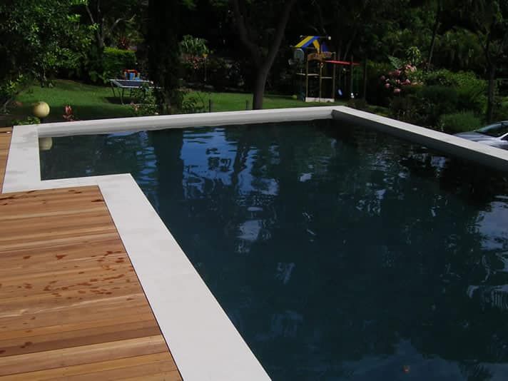 Pool With Dark Water, Light Concrete Border, and Wooden Deck — Mad Pool Interiors and Renovations in Baringa, QLD