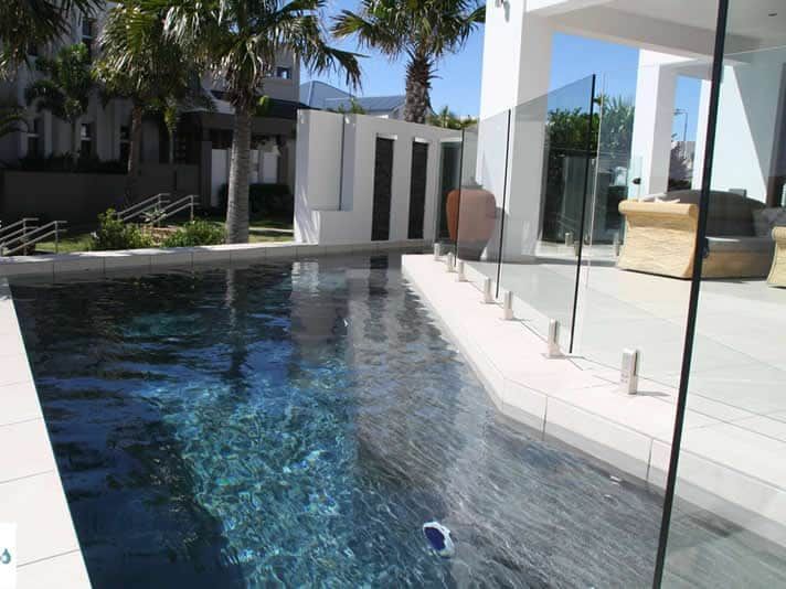 Pool With Dark Water, Glass Fence, White Tiles, Palm Trees — Mad Pool Interiors and Renovations in Baringa, QLD