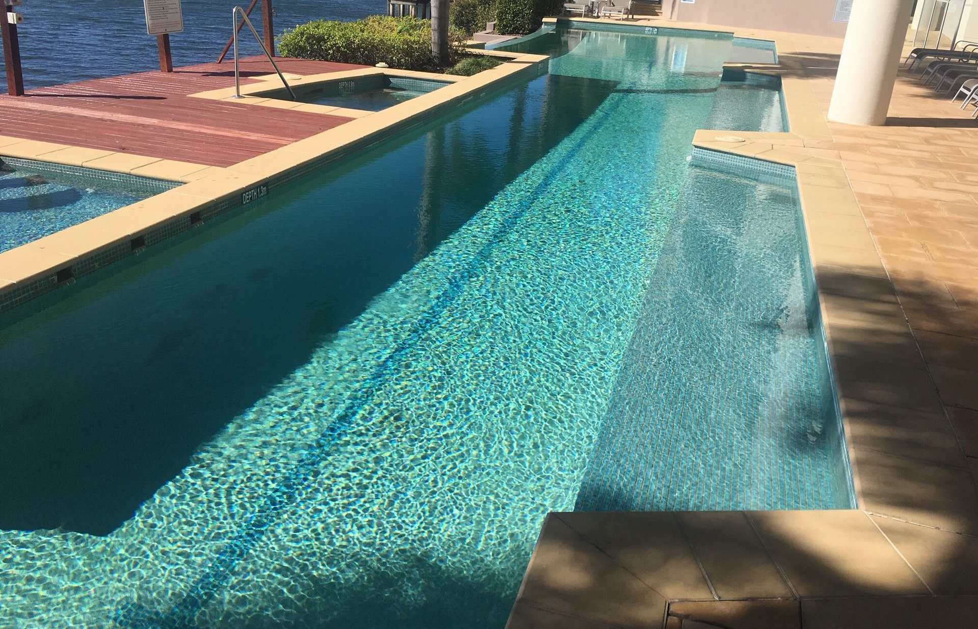 Long Outdoor Swimming Pool Beside a Wooden Deck — Mad Pool Interiors and Renovations in Baringa, QLD