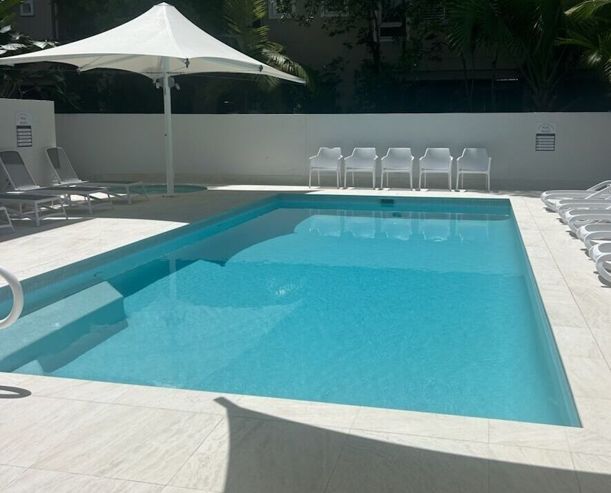 Pool With White Loungers, Umbrella, and Patio Seating — Mad Pool Interiors and Renovations in Baringa, QLD