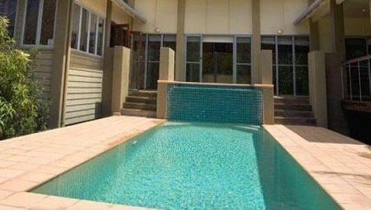 Backyard Pool With Turquoise Water and a Tiled Wall Beside a House — Mad Pool Interiors and Renovations in Baringa, QLD