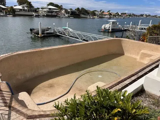 Empty Beige Boat With Docked Ramp Beside a Calm Waterfront Canal — Mad Pool Interiors and Renovations in Baringa, QLD
