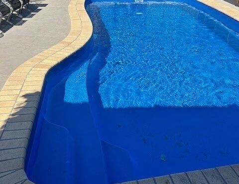Curved Backyard Swimming Pool With Blue Water and Beige Stone Deck — Mad Pool Interiors and Renovations in Baringa, QLD